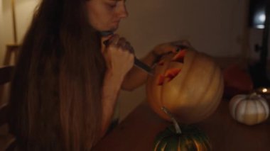 Uzun Saçlı Genç Esmer Mum Işığının Karanlığında Bir Balkabağı 'ndan Bir Balkabağı Oyuyordu. Masada Küçük Balkabakları.