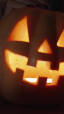 Dikey video. Karanlık Oda 'da, Jack-o' Lantern 'ın içine bakan kadın, Yüzü Alev' den gelen parlak ışık tarafından aydınlatılır. Lid 'le kapatıyor. Yavaş Hareket.