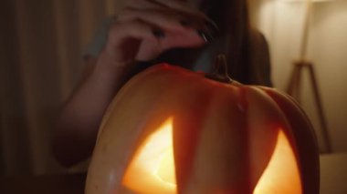 Balkabağı fenerinin içine bakan genç kadın, parlak mum ışığıyla aydınlatılıyor. Cadılar Bayramı Gecesi.