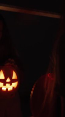 Dikey video. Karanlık Yatak Odası 'nda Aynanın Önündeki Kadın, Ilık Işık ve İçeriye Bakışlı Balkabağı Tutar, Lid' i Açar. Cadılar Bayramı Ritüeli kavramı.