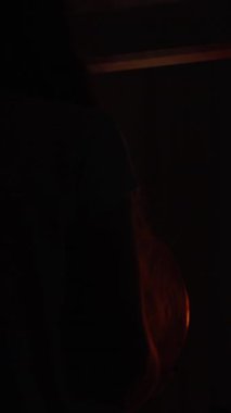 Dikey video. Uzun Saçlı Genç Bir Kadın, Aynanın Önündeki Karanlık Bir Odada Cadılar Bayramı Balkabağı Tutuyor, Lid 'i kaldırıyor ve parlak ışıkla yüzünü aydınlatıyor..