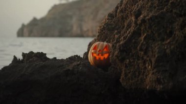 Cadılar Bayramı Balkabağı Jack-O 'Lantern Denizde Bir Kayanın Üzerinde Uzanıyor, Gözlerinden Işık Flaşları.