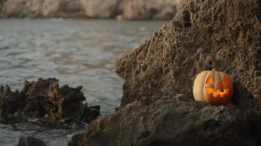 Dalgalar Kaya 'ya Karşı Jack-O' Lantern Balkabağı ve İçindeki Mum Alevi ile Çarpışıyor. Deniz kıyısındaki Cadılar Bayramı.