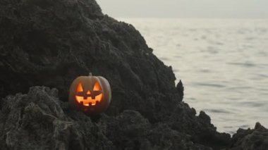 Balkabağı Jack-O 'Fenerli titreyen mum ışığıyla Deniz' deki Keskin Kayalıklarda Duruyor. Cadılar Bayramı Sahnesi.