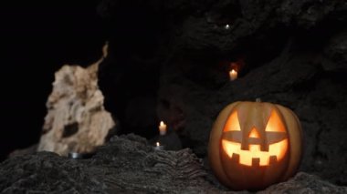 Jack-O 'Lantern Balkabağı, içinde mumlar olan karanlık bir mağarada Kayalıklarda Yanan Alevler İçinde Duruyor. Uzak Çıkış ve Işık Görünür. Cadılar Bayramı Arkaplanı.