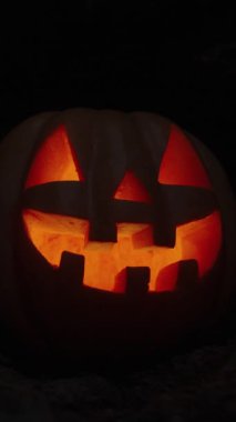 Dikey video. Cadılar Bayramı için balkabağı Jack-O 'Lantern Kayalıklardaki Karanlık Mağarada Yanan Işık ile. Uzakta mumlar, Azizler Günü için Statik Arkaplan.