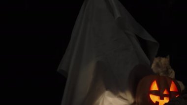 Beyaz çarşaflı bir şey karanlık bir mağarada oturuyor ve beni Jack-O 'Lantern Balkabağı ve yanan mumların yanında görüyor. Ürkütücü Cadılar Bayramı Arkaplanı.