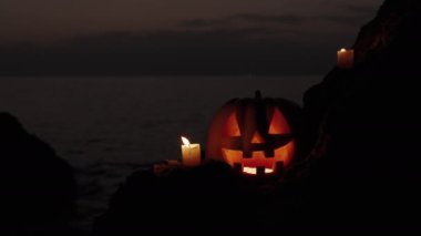 Cadılar Bayramı Gecesinde Parlayan Balkabağı Denizde Kayaların Üzerinde Duruyor. Mumlar Çemberde, Şenlikli Sunak, Arkaplan.