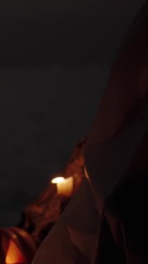 Dikey video. Cadılar Bayramı 'nda, balkabağı ve mumların yanında, Deniz kıyısındaki kayalıklarda beyaz çarşafta oturan bir şey. Balkabağı Lid 'i açar.