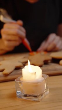 Dikey video. Bir kadın balkabağı şekilli zencefilli kurabiyeyi kremayla kaplıyor. Sıcak bir aile akşamı. Cadılar Bayramı Şenlik Masası.