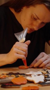 Dikey video. Aile Gecesi, Masadaki Mumlar ve Cadılar Bayramı temalı kurabiyeleri buzla süsleyen bir kadın. Sıcak Sinematik Işıklandırma.