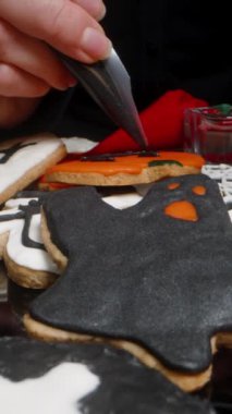 Dikey video. Balkabağı şekilli balkabağı şekilli bir Fener kurabiyesine siyah buzlu bir yüz çizmek. Cadılar Bayramı Sembollerinde Tematik Şekerler. Dolly Kaydırıcı, Yakın plan.