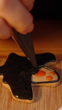 Dikey video. Siyah Buzlu ve Kırmızı Gözlü Ev Yapımı Hayalet Şeklinde Kurabiye. Cadılar Bayramı için Bir İkram.