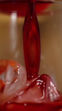 Dikey video. Buzlu bir bardağa kırmızı meyve suyu, ılık loş ışıklı bir akşam atmosferi..