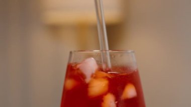 Soğuk Damlacıklarla kaplı, pipetle karıştırılmış, kırmızı içecekle kaplanmış bir bardak. Arkadaki Lambadan Ilık Işık.