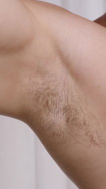 Dikey video. Gün boyunca yeni koltukaltların korunması her sabah için hayati bir adımdır. Burada, bir adam iyi aydınlatılmış bir banyoya deodorant sürüyor..