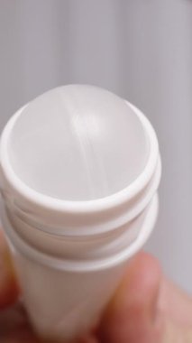 Dikey video. Yuvarlanan bir deodorantın ya da terleme önleyici maddesinin yakın çekimi, bir adam mekanizmayı göstermek için parmağıyla çevirir..