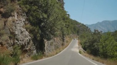 Rocky Kayalıkları ve Yoğun Ağaçlar 'dan geçen Dar Yol. Arabanın manzarası, uzak dağlara giden yolu gösteriyor, macera hissi yaratıyor. Açık Mavi Gökyüzü Yolculuğun Manzaralı Güzelliğini Geliştirir.