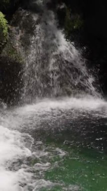 Dikey video. İkili Şelaleler Yosun kaplı kayaların üzerinden aşağıdaki havuza dökülüyor. Yeşillik şelaleyi sarar, dingin bir ortam yaratır ve doğal manzarayı tazeler..