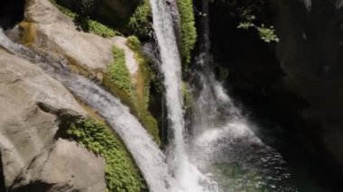 İkiz şelaleler yosunlu kayalıkların üzerinden aşşağıya, aşağıdaki temiz bir havuza dökülüyor. Yeşillik serinliği arttırır ve doğal manzarayı tazeler.