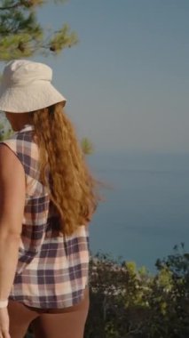 Dikey video. Uzak Vadi ve Yuvarlanan Tepeler 'in nefes kesici manzarasıyla Eski Harabelerde Yürüyen Bir Kadın Dağın dibinde deniz ve şehirle birlikte