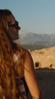 Dikey video. Majestic Mountain Views 'da, harabelerin arasında duran bir kadın, Öğleden Sonra' nın yumuşak ışığında yıkandı..