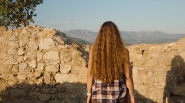 Tarihi harabelerde ayakta duran bir kadın manzaranın güzelliğine daldırılmış Geniş Dağ Sırasına bakıyor..