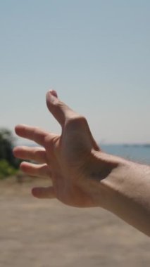 Dikey video. Bir adamın eli arabanın camından uzanıyor, Esintiyi hissediyor. Açık Mavi Gökyüzü ve Arkaplanda Okyanus Sahil Yolculuğu sırasında basit bir sevinç anı yakalayan dingin ve ferahlatıcı bir sahne oluşturur..