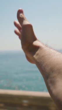 Dikey video. Araba penceresinden uzanan bir el, esintinin tadını çıkarıyor. Okyanus ve çiçek açan çalılar güzel bir sahil manzarası yaratır. Bu, Deniz kenarındaki Yolculuğun Neşe ve Özgürlüğünü Yakalıyor.