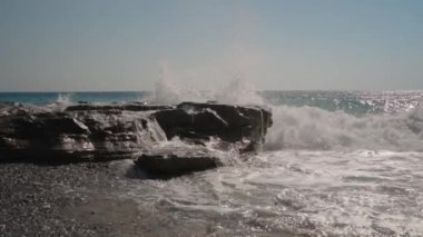 Dalgalar sahile çarparken Rocky Ledges 'in üzerinde çağlayan sular. Köpük ve Sis, Güneş Işığı Okyanusu ve Açık Mavi Gökyüzü tarafından geliştirilmiş dramatik, dinamik bir sahne yaratır..