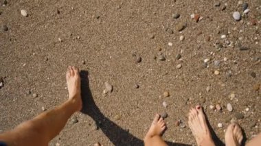 Çakıl Kumsalında Çıplak Ayaklı Bir Aile. Güneş ışığı, Kum yüzeyindeki adımlarını vurguluyor, Huzurlu ve rahatlatıcı bir sahne yaratıyor.