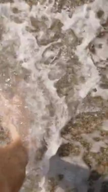 Dikey video. Dalgalarla Islak Kumda Yürüyen Bir Adamın Ayakları. Yavaş Çekim Efekti Doğayla Bağlantıyı ve Sahil Yürüyüşünün Huzurlu Ritmini Vurguluyor.