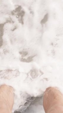 Dikey video. Çıplak Ayaklar Islak Kuma Batar Köpüklü Dalgalar Kumsalda Nazikçe Kucaklaşır Huzurlu Kıyı Anı Oluşturur.