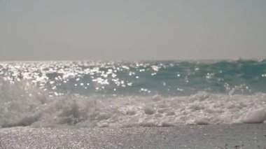 Güneş Dalgaları Okyanus yüzeyinde dans eder, Kumsala yaklaşan Parlayan Işığı yansıtır.