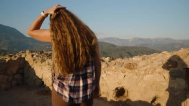 Tarihi harabelerde gezinen kadın, Görkemli Dağ Manzaralarını Yumuşak Akşam Güneşi Altında Aldı.