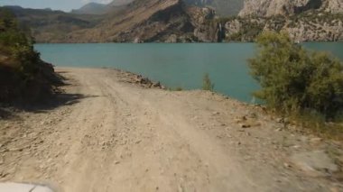 Çamur Yolu, Serene Gölü 'nün yanında uzanır. Arka plandaki engebeli dağ manzarası. Huzurlu bir yolculuk için yavaş çekimde yakalanır..
