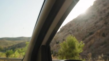 Güneş Işığı Araba Penceresinden Geçer, İçini Aydınlatır, Engebeli Tepeler ve Dışarıdaki Yeşillik, Sahne Sürüşü 'nde Huzur Anı Yakalar.