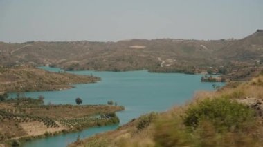 Serene Gölü Engebeli Arazide Dönüyor, Çerçevelenmiş Arid Tepeleri ve Araba Penceresinden Açık Gökyüzü.
