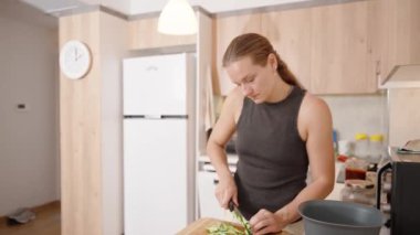Mutfakta, genç bir kadın dikkatle salatalıkları kesiyor..
