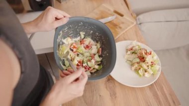 Salatayı dikkatlice kaplayan genç kadın sağlıklı bir tabağa hizmet etmeye hazırlanıyor..