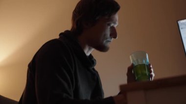 Gece Hiddeti, genç bir adam yeşil bir içecek yudumluyor. Ciddi duruşu, işe odaklandığını vurguluyor.