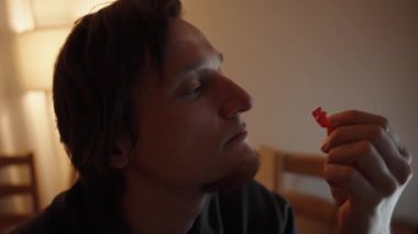 Dalgın bakışlar, genç bir adam jelibon ayısını inceliyor. Yumuşak ışıklandırma merakını vurguluyor..