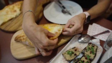 Khachapuri 'nin tadını çıkaran genç bir kadın hamuru yapışkan yumurta ve peynire batırıyor. Bu Adjarian yemeği mükemmel bir lezzet karışımı sunar..