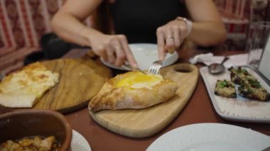 Khachapuri 'yi kesen genç bir kadın zengin ve peynirli dolgunun tadını çıkarmaya hazırlanıyor. Geleneksel ekmek ve yumurta kombinasyonu karşı konulmazdır..