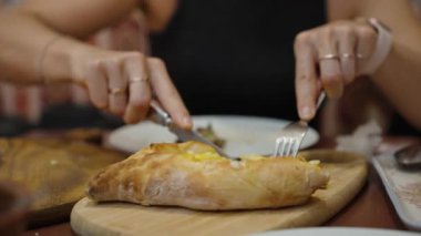 Khachapuri 'yi kesen genç bir kadın dikkatlice altın hamuru kesiyor. Zengin, peynirli dolgu lezzetli bir tat vaat ediyor..