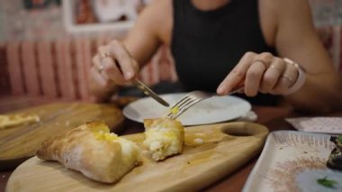 Khachapuri 'ye yakın planda, genç bir kadın peynirin merkezini kesiyor. Zengin, geleneksel tatlar onu lezzetli bir seçim yapar..