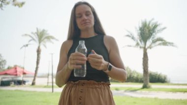Serinletici bir an, genç bir kadın yemyeşil bir parkta su içiyor. Güzel bir çevre onu mükemmel bir kırılma yapar..