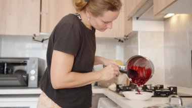 Tencereden bir kaseye canlı kiraz kırmızısı sosu dökerek, Tarifte Anahtar Adım 'ı tamamlamak. Mutfağın Parlak Ortamı Mutfak Odağını Artırır.