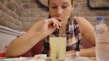 Kadın, Cozy Cafe 'de pipetle serinletici bir içecekten zevk alıyor, Tuğla Duvarlar Büyüleyici Atmosfere ekleniyor.