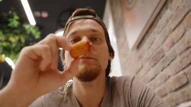 Cap 'teki Adam Peynirli Atıştırmalık Tutuyor, Tuhaf bir ifadeyle Stringy Cheese' i Gözlüyor.